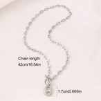 Collier Grains de Café en acier inoxydable doré, fermoir toggle, posé sur un tissu blanc et une pierre texturée, Maison Mercier.