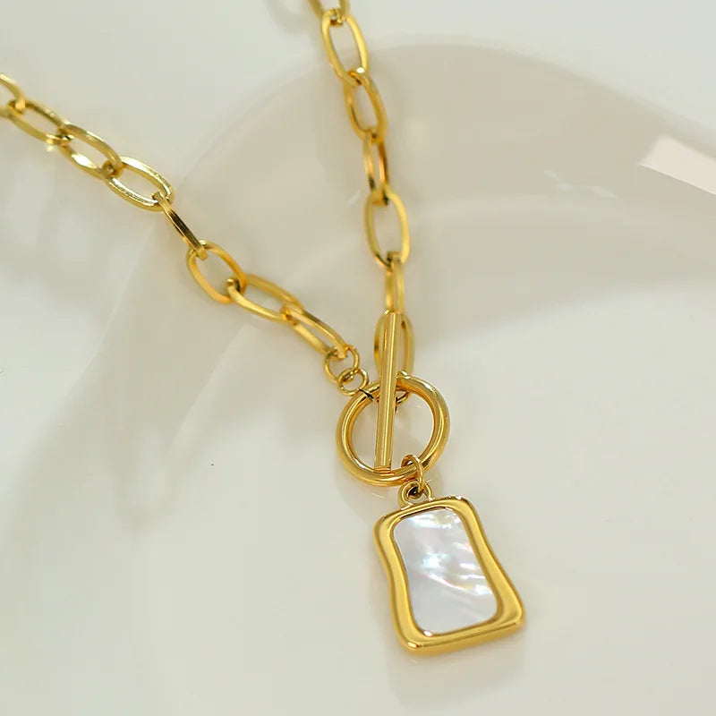 Gros plan sur le pendentif en nacre naturelle et le fermoir T-bar d'un collier doré, Maison Mercier.