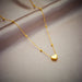 Détail d'un collier pendentif cœur 'Love' en acier inoxydable doré poli, posé sur un tissu élégant, Maison Mercier.