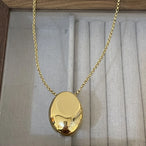 Collier pendentif ovale sculptural poli en finition dorée, suspendu dans un écrin de présentation, Maison Mercier.