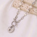 Collier Grains de Café en acier inoxydable argenté, fermoir toggle, présenté sur un fond blanc et une surface minérale, Maison Mercier.