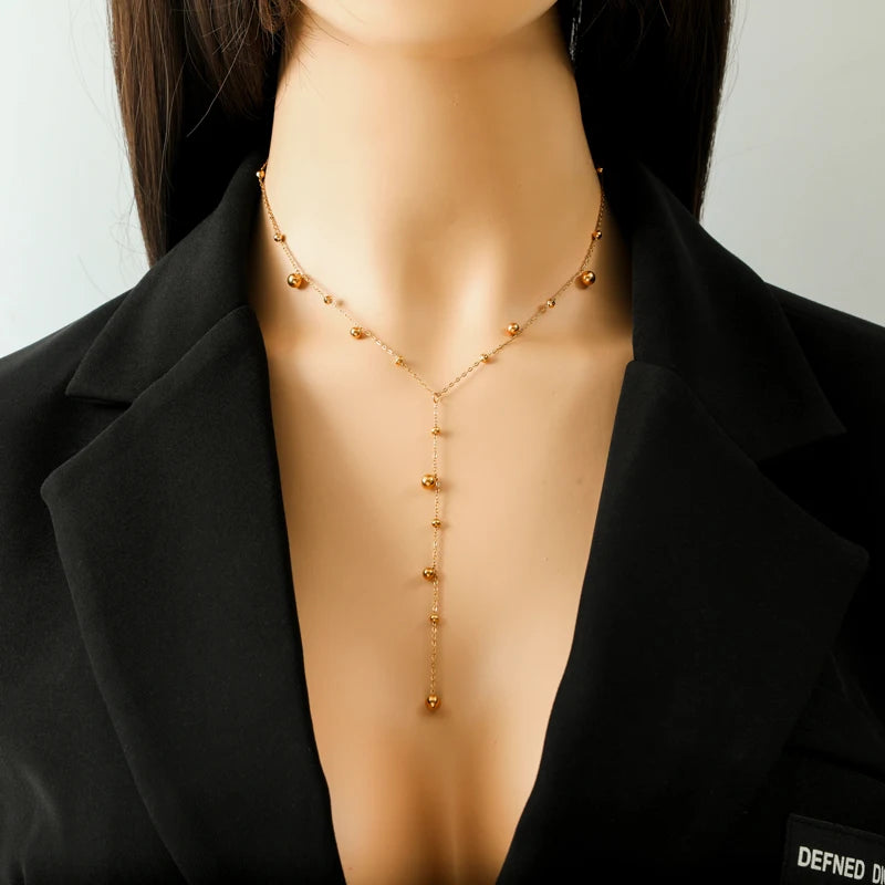Modèle portant le collier lariat Y à perles rondes dorées sur un décolleté, mettant en valeur son élégance et sa longueur.