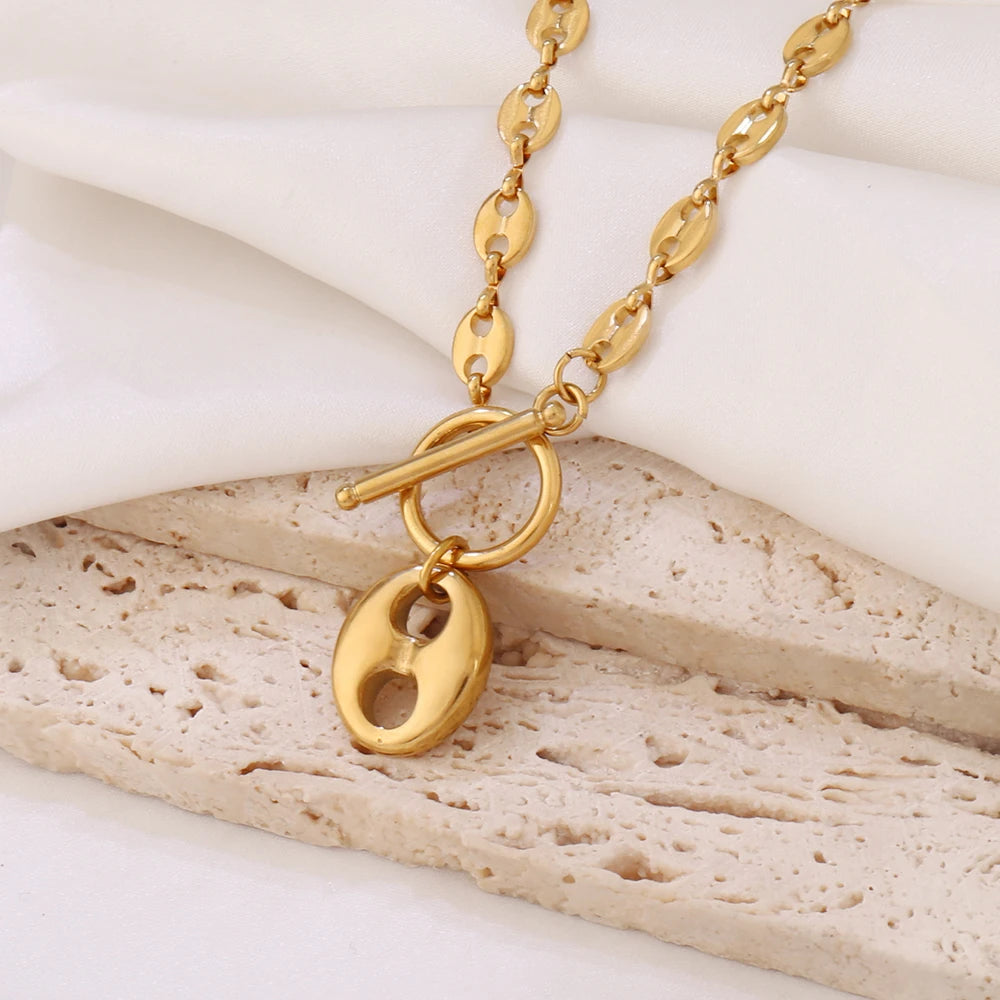 Détail du fermoir toggle et du pendentif ovale du Collier Grains de Café en acier inoxydable doré, Maison Mercier.