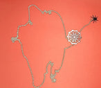 Collier pendentif toile d'araignée et araignée en finition argentée, la chaîne délicatement posée sur un fond corail, Maison Mercier.