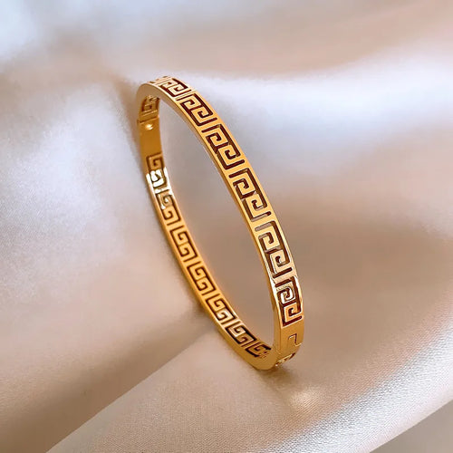 Détail d'un bracelet jonc rigide en acier doré, orné du motif Méandre Grec, présenté sur un drapé de soie blanche, Maison Mercier.