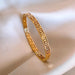 Détail d'un bracelet jonc rigide en acier doré, orné du motif Méandre Grec, présenté sur un drapé de soie blanche, Maison Mercier.