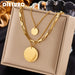 Détail d'un collier superposé doré avec maillons rectangulaires et disques polis, présenté sur un écrin beige, Maison Mercier.