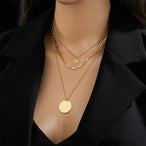 Gros plan sur les maillons rectangulaires et le grand disque poli d'un collier doré, Maison Mercier.