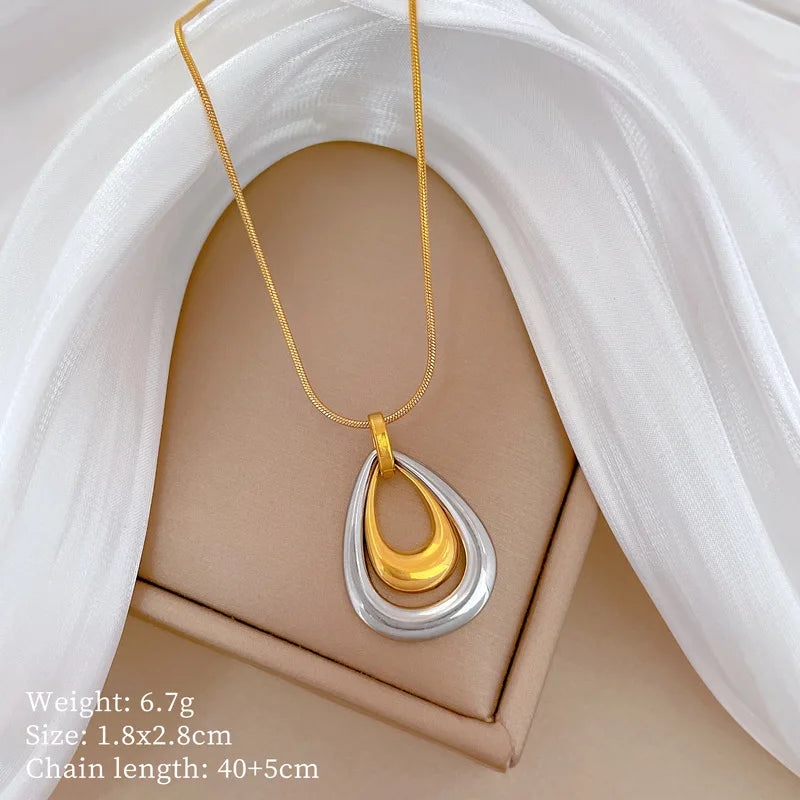 Vue d'ensemble du collier pendentif double goutte bicolore en acier inoxydable poli, or et argent, présenté sur un écrin.