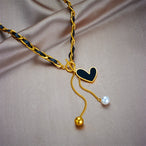 Détail d'un collier pendentif cœur 'Love' en acier inoxydable doré poli, posé sur un tissu élégant, Maison Mercier.