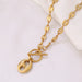 Collier Grains de Café en acier inoxydable doré, fermoir toggle, posé sur un tissu blanc et une pierre texturée, Maison Mercier.