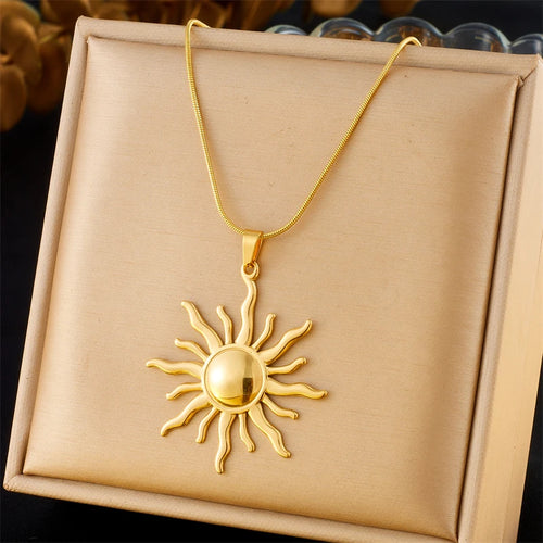 Détail d'un collier pendentif soleil rayonnant en acier inoxydable doré, présenté sur un écrin beige, Maison Mercier.