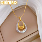 Détail d'un collier pendentif double goutte bicolore en acier inoxydable poli, or et argent, sur fond crème.