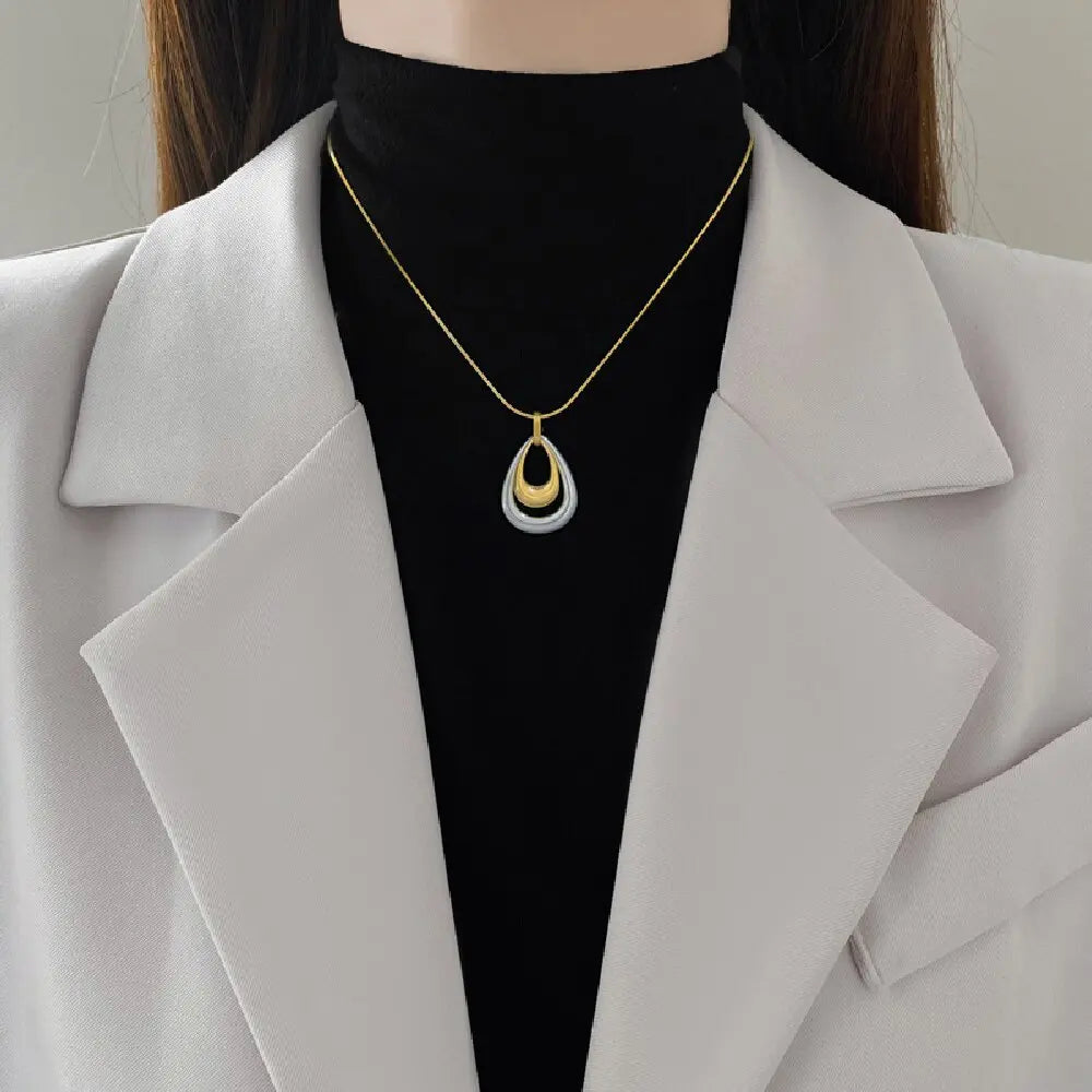 Pendentif bicolore en acier inoxydable, capturant la lumière avec ses finitions or et argent.