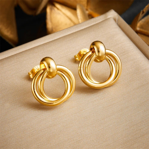 Détail d'une collection de boucles d'oreilles variées en acier inoxydable doré, présentant des designs géométriques, perlés et organiques, Maison Mercier.