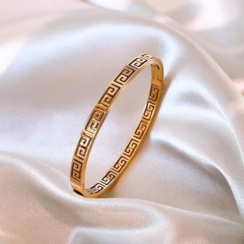 Vue rapprochée d'un bracelet jonc unisexe en acier inoxydable doré, mettant en lumière la finesse du motif grec antique, Maison Mercier.