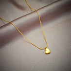 Détail d'un collier pendentif cœur 'Love' en acier inoxydable doré poli, posé sur un tissu élégant, Maison Mercier.