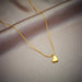 Détail d'un collier pendentif cœur 'Love' en acier inoxydable doré poli, posé sur un tissu élégant, Maison Mercier.