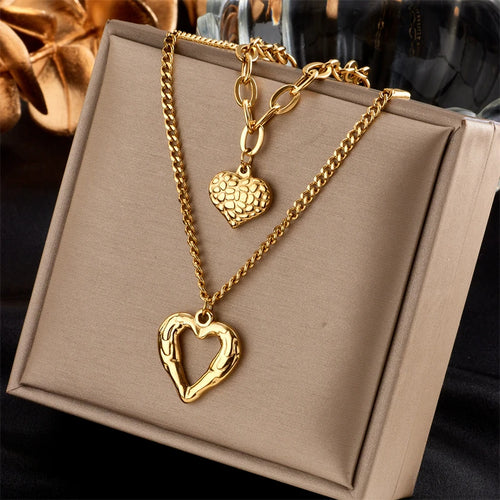 Détail d'un collier pendentif cœur 'Love' en acier inoxydable doré poli, posé sur un tissu élégant, Maison Mercier.