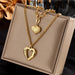 Détail d'un collier pendentif cœur 'Love' en acier inoxydable doré poli, posé sur un tissu élégant, Maison Mercier.