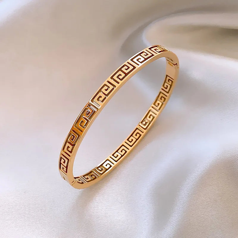 Bracelet jonc doré avec motif Méandre, capturant la lumière sur sa surface polie, symbolisant l'élégance intemporelle, Maison Mercier.