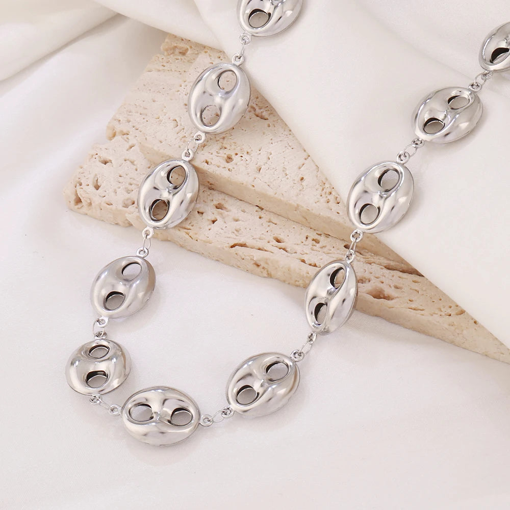 Collier chaîne grains de café en acier inoxydable finition argenté, élégamment posé sur un drapé blanc.