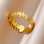 Photographie d'une bague ajustable dorée en acier inoxydable, au design original en forme d'arête de poisson stylisée, Maison Mercier.