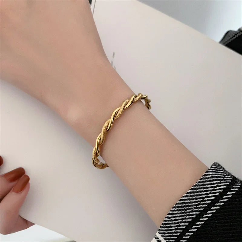 Bracelet jonc ouvert torsadé doré en acier inoxydable, présenté dans un écrin de velours rouge, avec une étiquette Saint Laurent et une carte Joyful Nails Studio.
