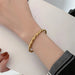 Bracelet jonc ouvert torsadé doré en acier inoxydable, présenté dans un écrin de velours rouge, avec une étiquette Saint Laurent et une carte Joyful Nails Studio.