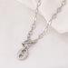 Collier Grains de Café en acier inoxydable doré, fermoir toggle, posé sur un tissu blanc et une pierre texturée, Maison Mercier.