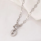 Collier Grains de Café en acier inoxydable doré, fermoir toggle, posé sur un tissu blanc et une pierre texturée, Maison Mercier.