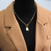 Collier chaîne dorée et pendentif nacre porté avec élégance sur une tenue camel et noire, Maison Mercier.