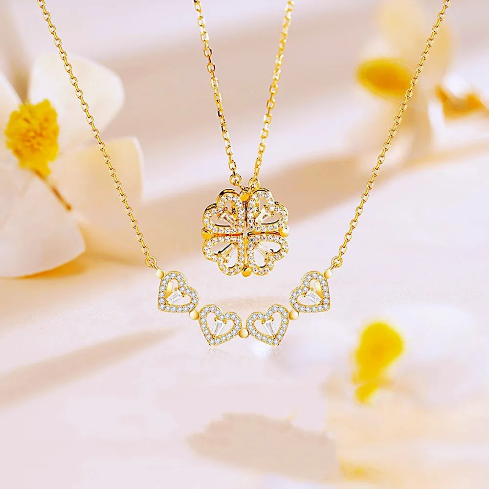 Duo de colliers pendentifs cœurs trèfle en acier doré et zirconia, l'un en forme de trèfle et l'autre en ligne de cœurs, sur fond clair fleuri, Maison Mercier.