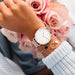 Montre féminine Maison Mercier, cadran noir épuré, bracelet maille milanaise finition or rose, portée au poignet avec un bracelet délicat à perles dorées.