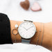 Montre féminine Maison Mercier, cadran blanc immaculé, bracelet maille milanaise en acier argenté, portée au poignet avec des bracelets argentés élégants, dont un avec un cercle et une pierre blanche.