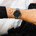 Montre féminine Maison Mercier, cadran noir minimaliste, bracelet maille milanaise en acier argenté, portée au poignet avec des bracelets fins argentés assortis.