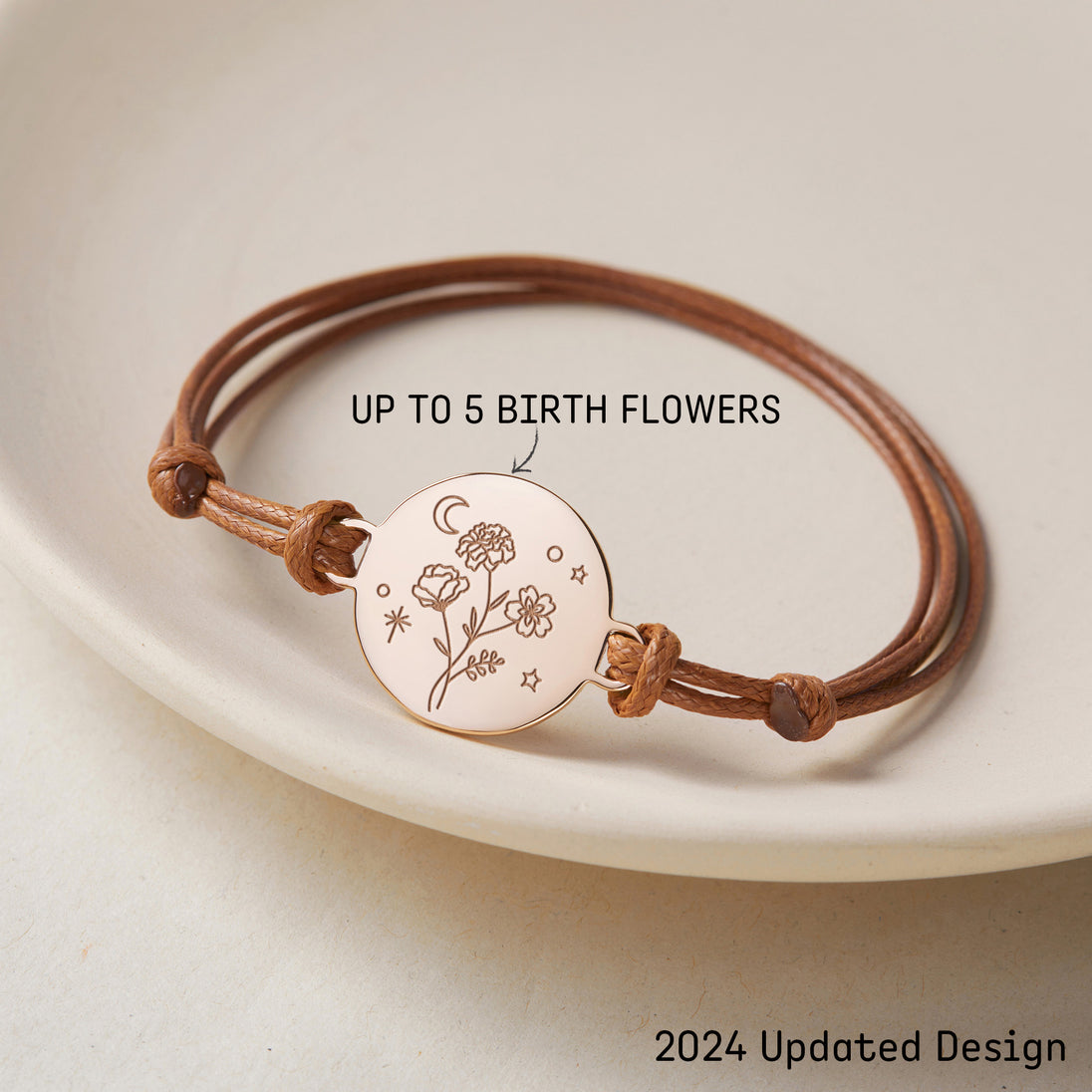 Bracelet cordon ajustable avec médaillon plaqué or gravé de fleurs de naissance, un croissant de lune et des étoiles, sur fond clair, avec texte "UP TO 5 BIRTH FLOWERS" indiquant la personnalisation.