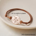 Bracelet cordon ajustable avec médaillon plaqué or gravé de fleurs de naissance, un croissant de lune et des étoiles, sur fond clair, avec texte "UP TO 5 BIRTH FLOWERS" indiquant la personnalisation.