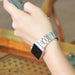 Vue d'un poignet portant un bracelet de montre à maillons classiques en acier inoxydable brossé argenté, la personne tenant un téléphone, dans un cadre lumineux et naturel, Maison Mercier.