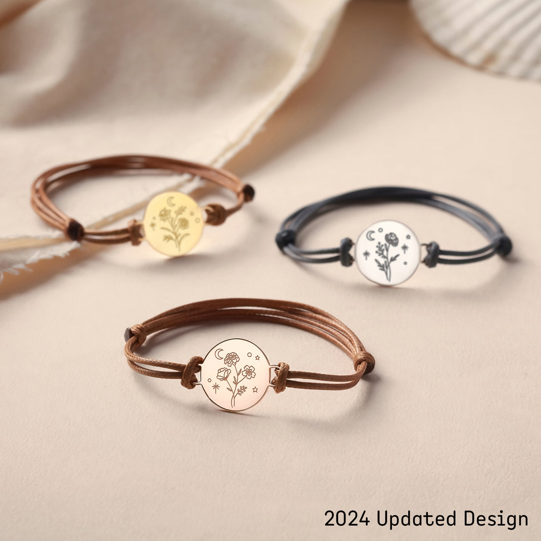 Assortiment de trois bracelets cordons ajustables, avec médaillons gravés en finitions or, or rose et argent, disposés élégamment sur un fond beige, illustrant les différentes options de personnalisation et de couleur.