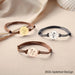 Assortiment de trois bracelets cordons ajustables, avec médaillons gravés en finitions or, or rose et argent, disposés élégamment sur un fond beige, illustrant les différentes options de personnalisation et de couleur.