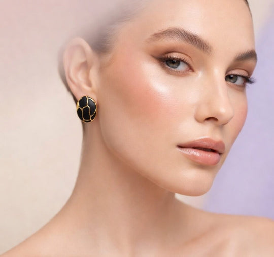 Portrait d'une femme portant une boucle d'oreille ovale en émail noir profond et finition or patiné, motif organique, mettant en valeur son élégance naturelle, Maison Mercier.