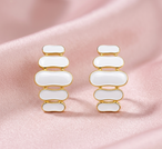 Détail d'une paire de boucles d'oreilles pendantes à maillons oblongs émaillés blanc pur, finition or précieux, sur fond noir scintillant, Maison Mercier.