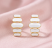 Détail d'une paire de boucles d'oreilles pendantes à maillons oblongs émaillés blanc pur, finition or précieux, sur fond noir scintillant, Maison Mercier.