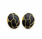 Vue de dessus d'une paire de boucles d'oreilles ovales en émail noir profond et finition or patiné, motif organique, sur fond blanc pur, Maison Mercier.