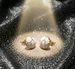 Détail d'une paire de boucles d'oreilles puces rondes en émail blanc et motifs dorés, posées sur un drapé de soie rose pâle, Maison Mercier.