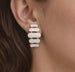 Détail d'une paire de boucles d'oreilles pendantes à maillons oblongs émaillés blanc pur, finition or précieux, sur fond noir scintillant, Maison Mercier.