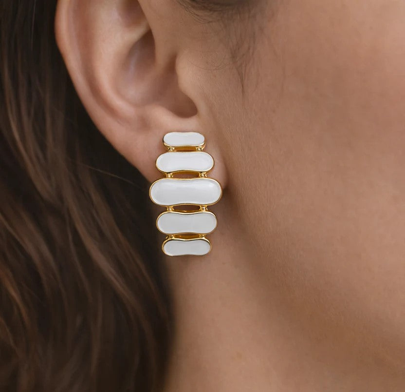 Détail d'une paire de boucles d'oreilles pendantes à maillons oblongs émaillés blanc pur, finition or précieux, sur fond noir scintillant, Maison Mercier.