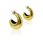 Détail d'une paire de boucles d'oreilles créoles bombées en acier doré poli, reflétant la lumière sur fond blanc.