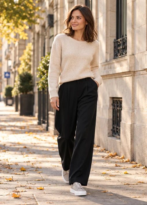 Une femme adulte portant Pull Vero Moda beige femme, Pantalon Vero Moda noir femme, Baskets Calvin Klein blanc femme. Matin en ville. Mise en scène IA illustrative.